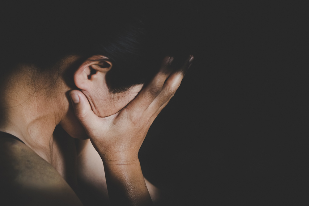 Young female assault victim hiding her face against a black background