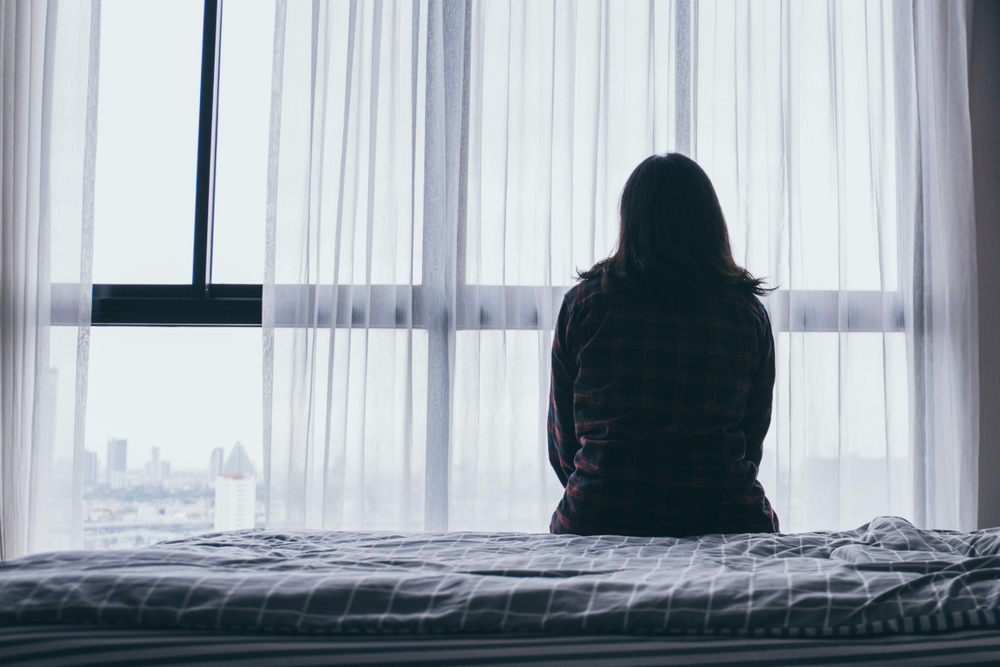 Silhouette of sexual abuse victim sat alone on a bed, looking out the window