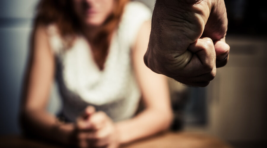 Young woman sat at a table in fear of domestic abuse, with a clenched fist in the foreground