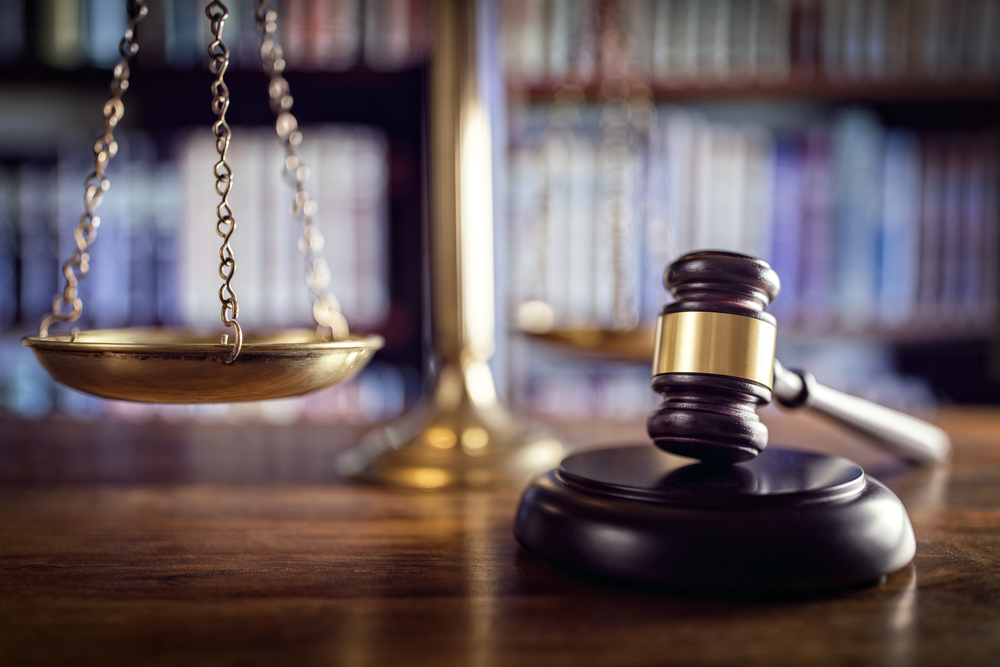 Close-up of judge gavel and scales of justice, with an array of books in the blurred background