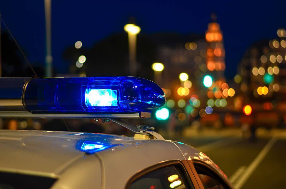 Upclose picture of a flashing light on top of a police car against the background of blurred city lights