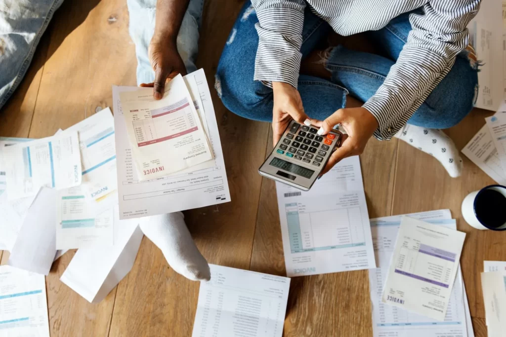Couple sat on the floor managing their debt, surrounded by papers and a calculator