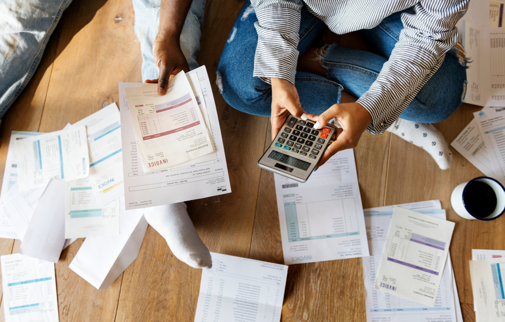 Couple sat on the floor managing their debt, surrounded by papers and a calculator