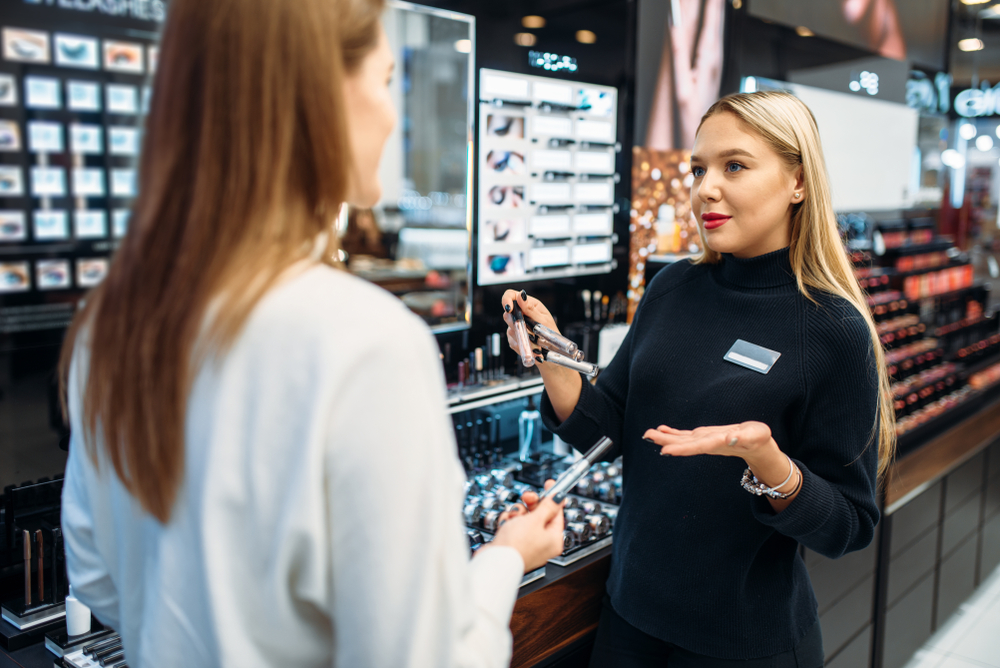 Photograph of shopping assistant talking to a customer about makeup in front of makeup stand