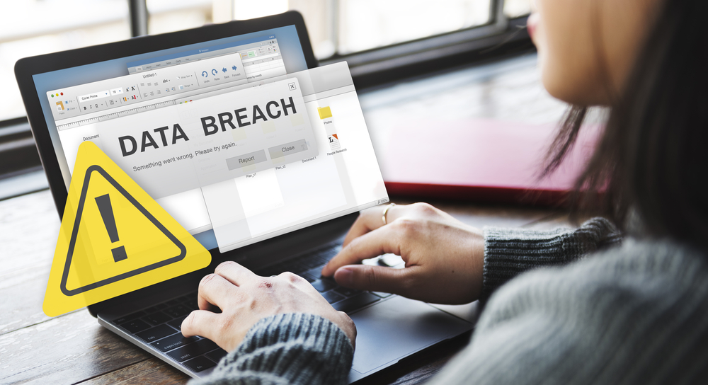 Woman sat at her laptop which displays an alert for a recent data breach