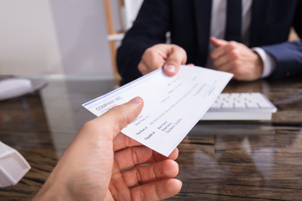 Photograph of man in suit and tie handing someone a cheque of compensation