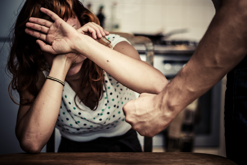 Woman sat at table covering her face in fear of domestic violence