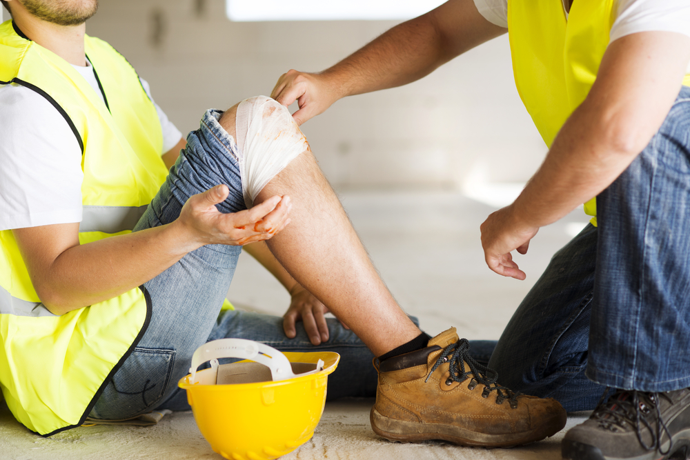 Photograph of a builder in high vis suit tending to a colleague who injured his knee at work