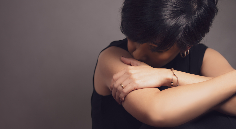 Photograph of a woman curled up, hiding her face after experiencing domestic abuse