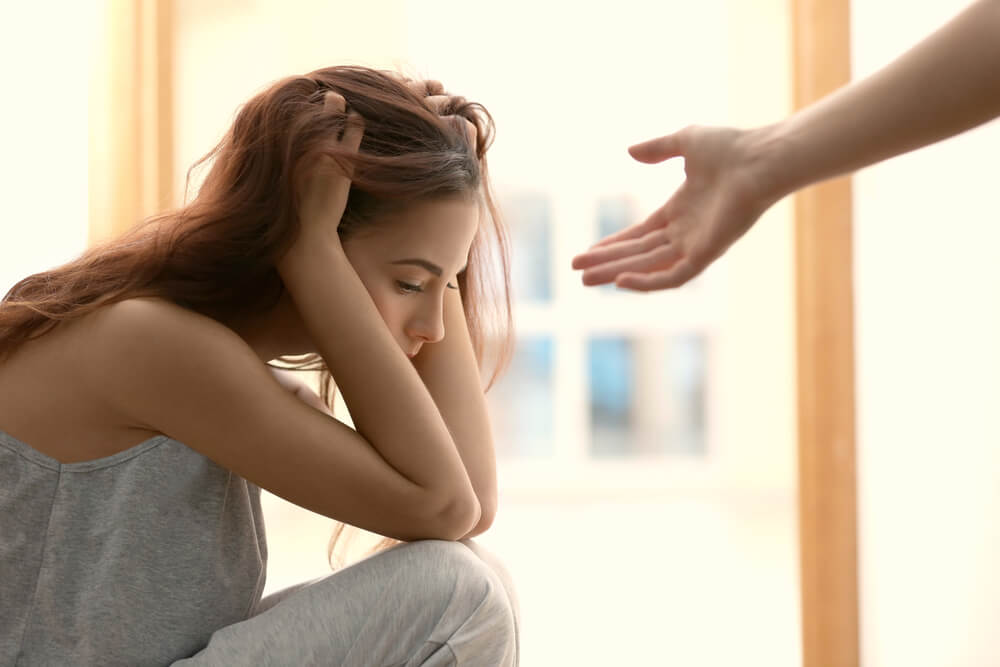 Victim of psychological assault on the floor with her hands to her head, and helpful arm out of frame reaching to help