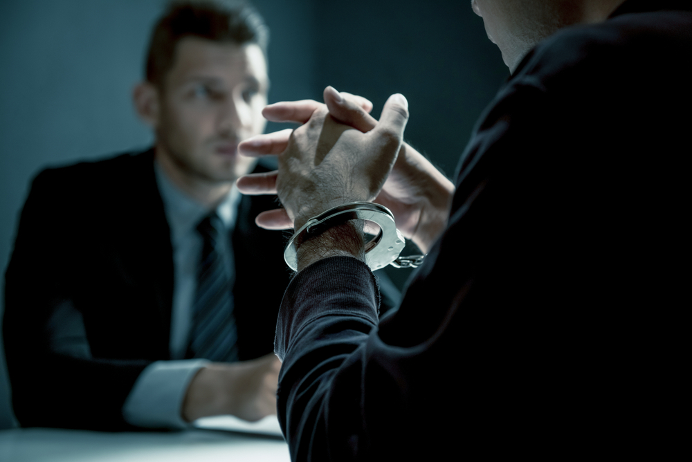 Photograph of man being interrogated in a dimly lit room whilst in handcuffs