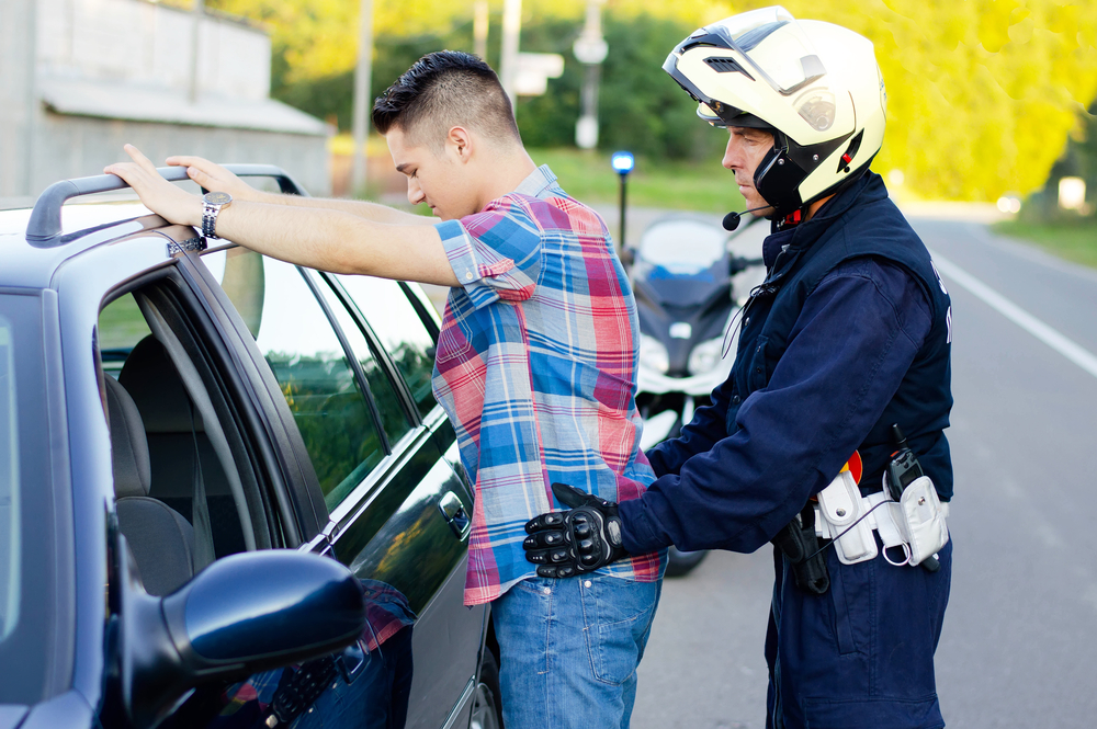 Photograph of motorcycle policeman stopping and searching driver on the side of the road 