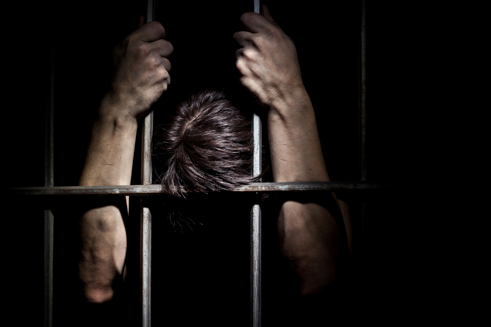 Photograph of man in jail cell with his head and arms against the bars after malicious prosecution