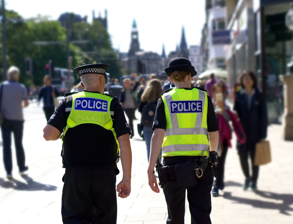 Policeman and policewoman patrolling town with people walking nearby