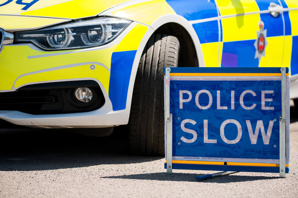 Police car next to a blue "police slow" sign 