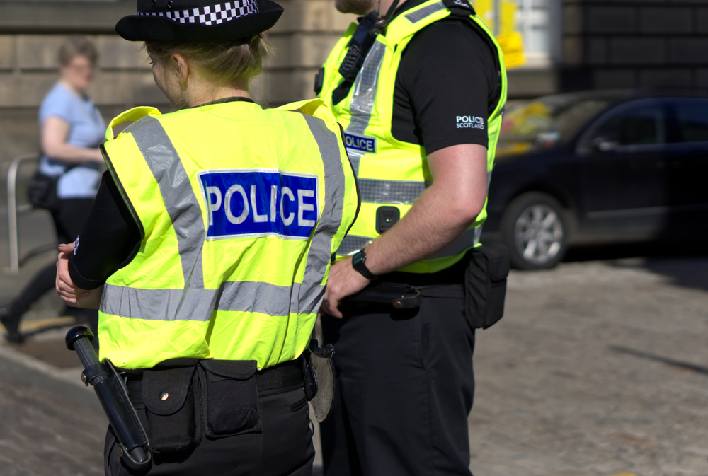 Policeman and Policewoman stood side by side in high visibility jackets with their backs to the camera