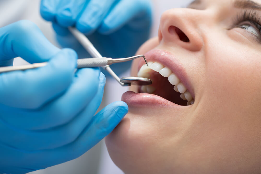 Photograph of a woman at a dentist appointment with tools touching her teeth