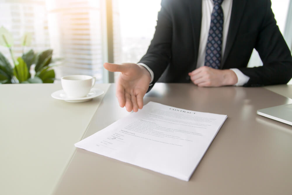 Photograph of a solicitor sat at a table with a contract about the british dental association data breach, stretching his man out to shake