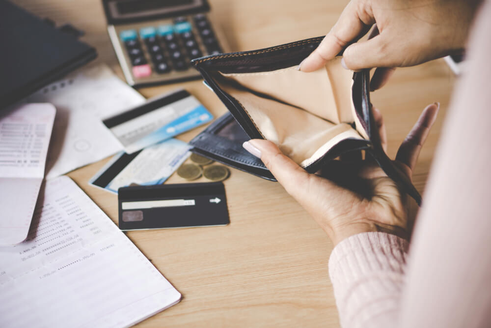 Woman looking through her empty wallet, with a calculator, forms and various cards on the desk to prove loss of earnings