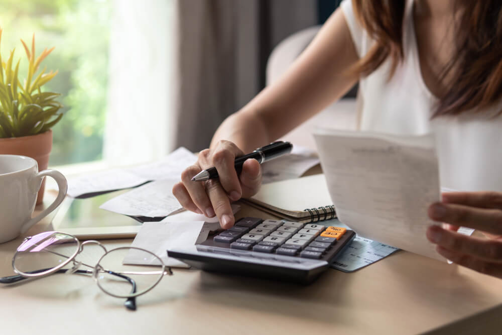 Woman calculating loss of earnings with calculator, various forms and her glasses on a desk