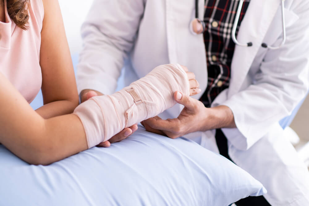 Bone specialist checking over patient's broken arm to assess potential self employed income loss