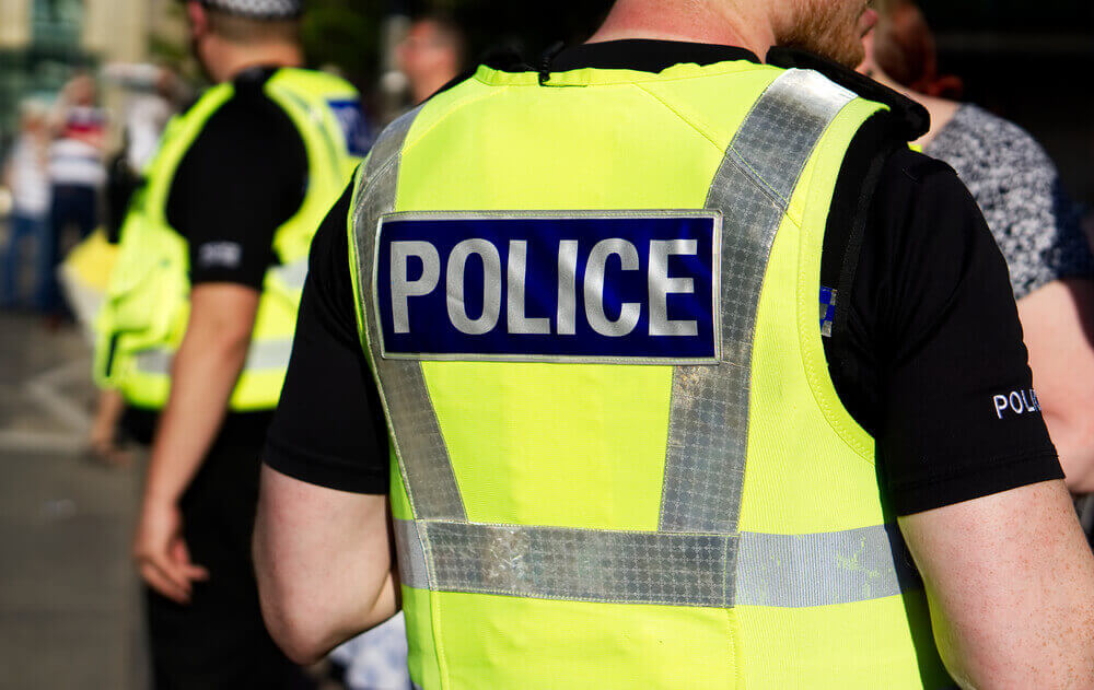 Colour image showing two police officers on duty during an event. Both officers are wearing hi-visibility vests with the word police on the back.