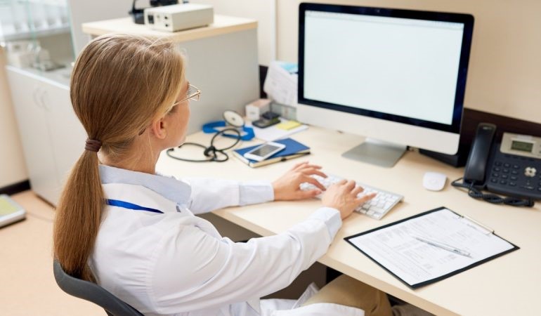 Photograph of female doctor with forms and laptop searching for the COVID-19 patients data breach