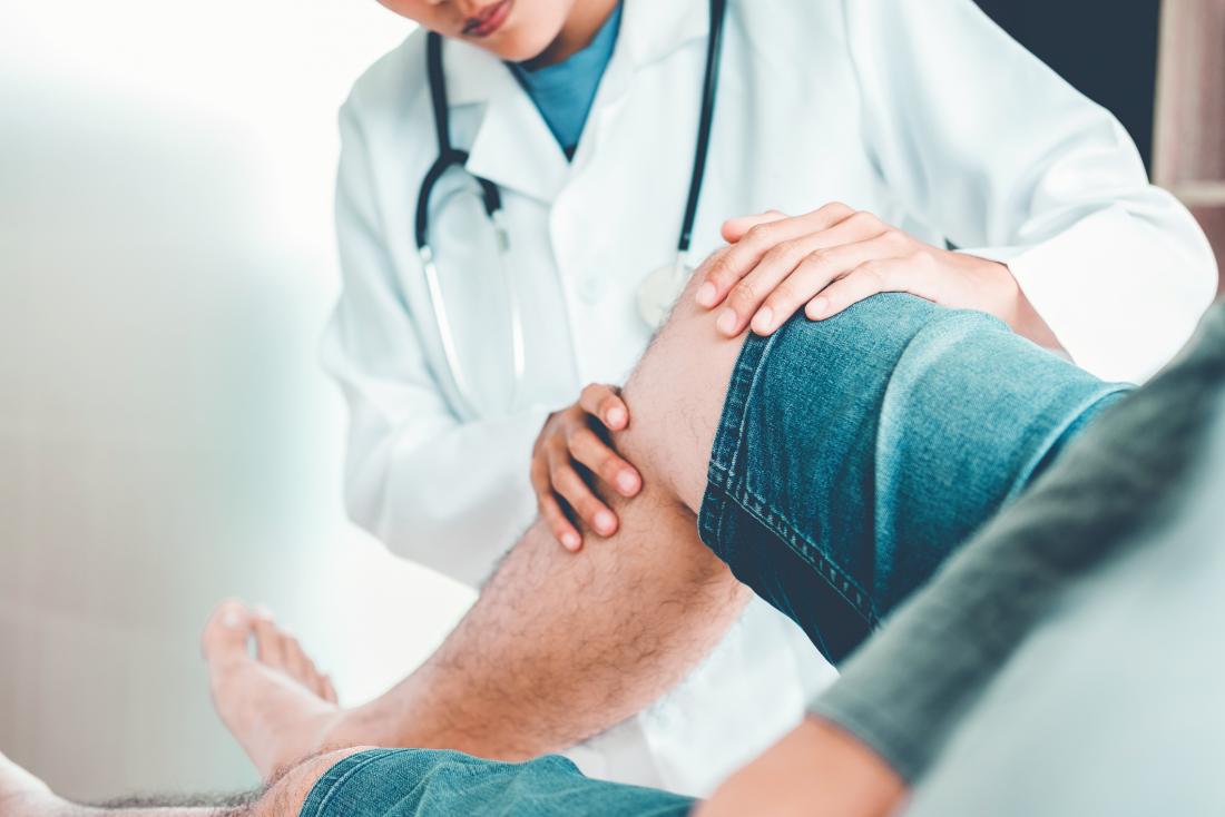 Doctor giving medical assistance to a man with a damaged knee after a road traffic accident