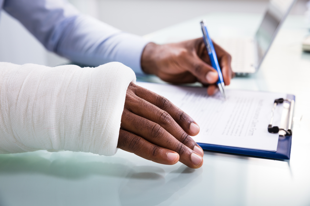 Close up photograph of a woman with her arm in a cast, signing a personal injury claim