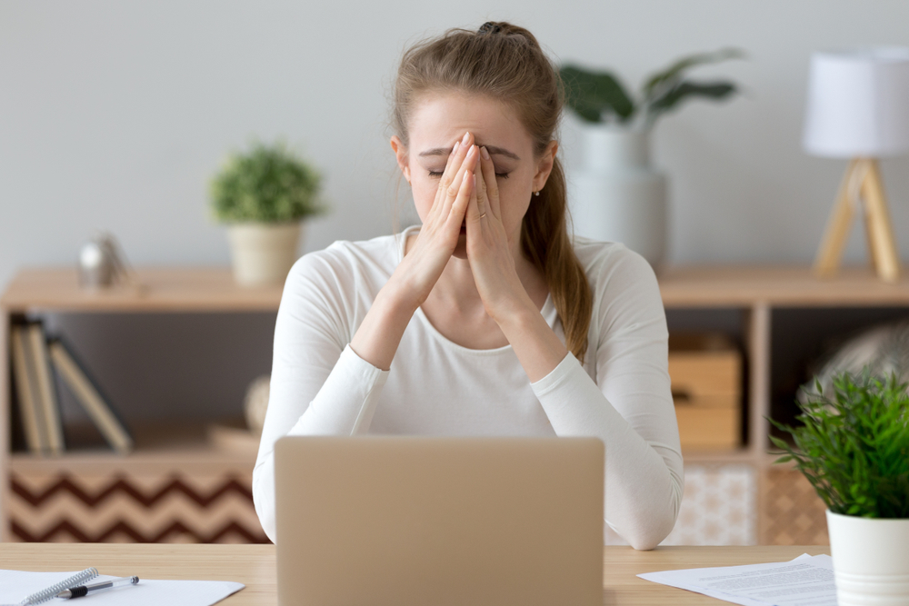 Sad female university student working from home during lockdown with her head in her hands at her laptop