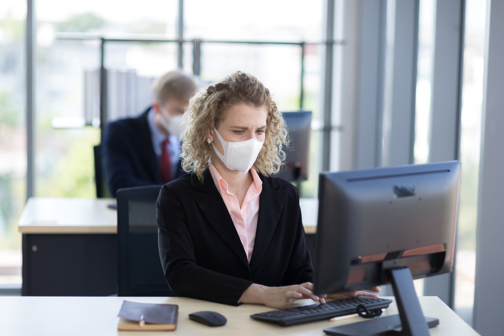 Blonde woman with curly hair working at her laptop wearing a COVID surgical mask