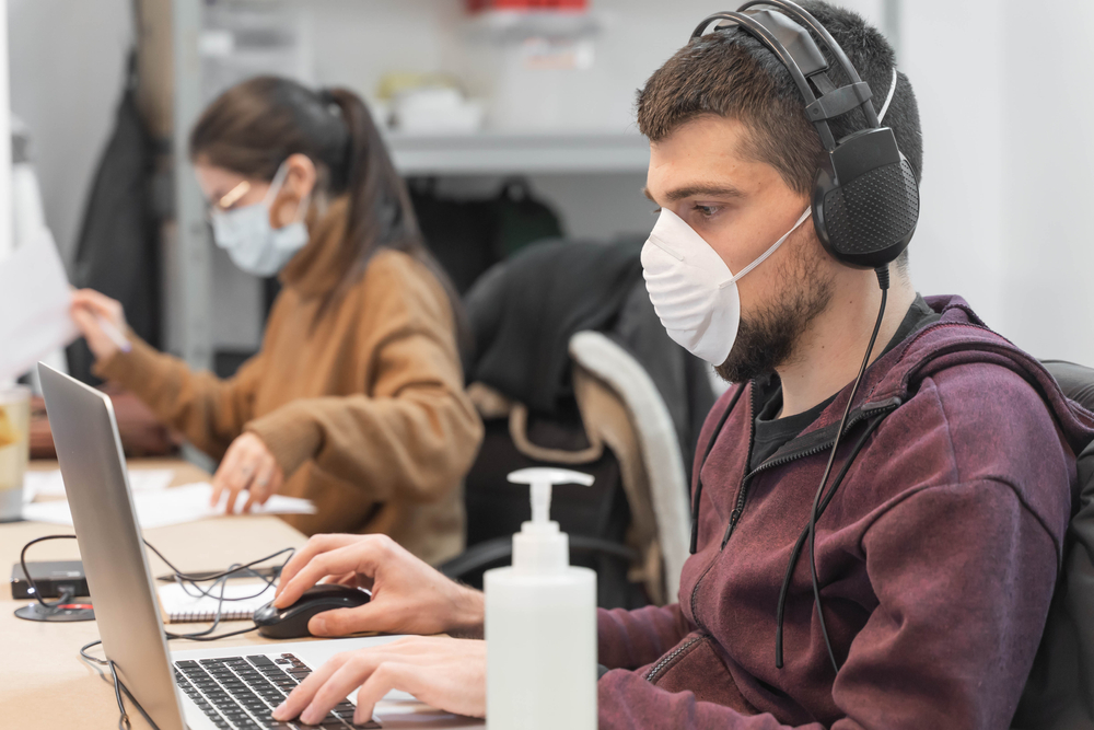 Photograph of call centre employees at work with PPE and COVID protection equipment at their desks