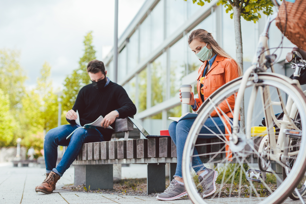 Photograph of a woman and man university student wearing masks and studying outside whilst socially distanced