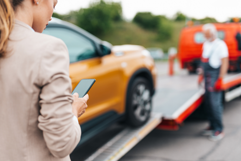 Photograph of woman calling tow truck for her orange damaged car 