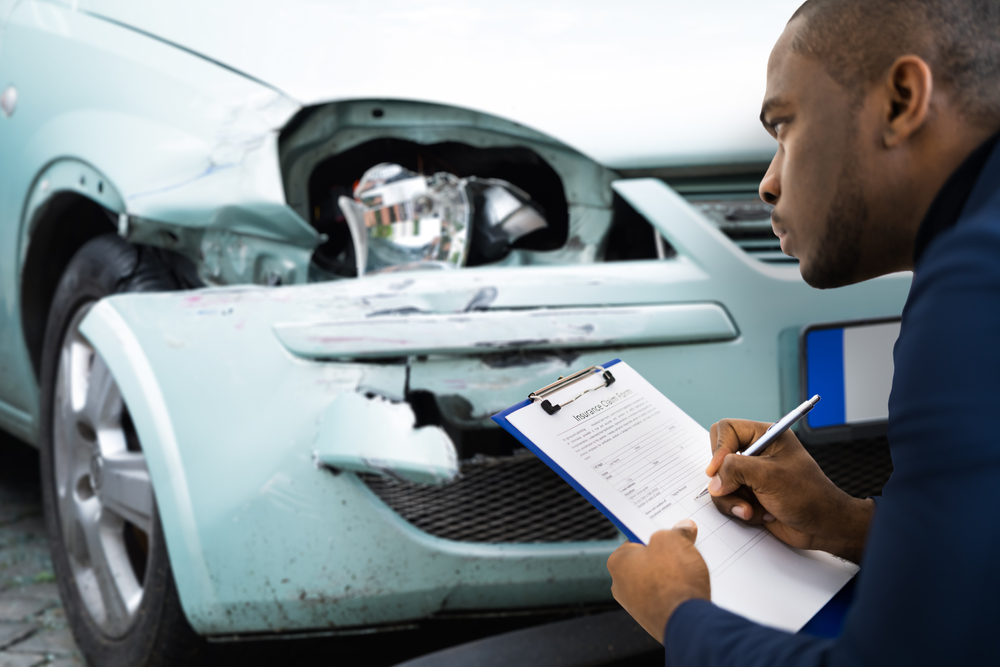 Insurance man in blue suit taking notes on the damage of a car