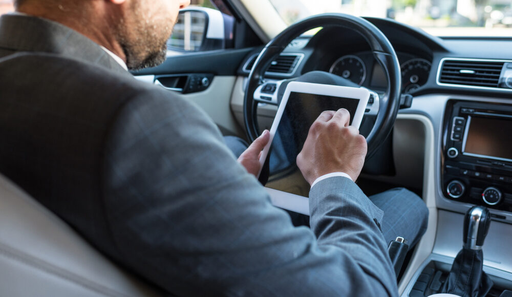 Photograph of man in suit video calling on his tablet whilst driving
