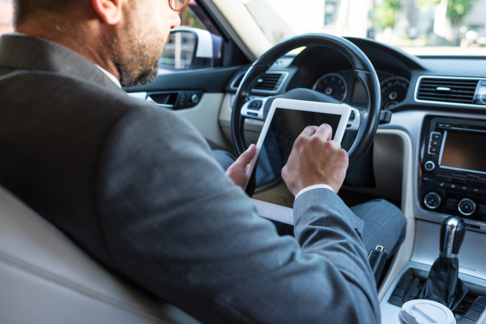 Photograph of man in suit video calling on his tablet whilst driving