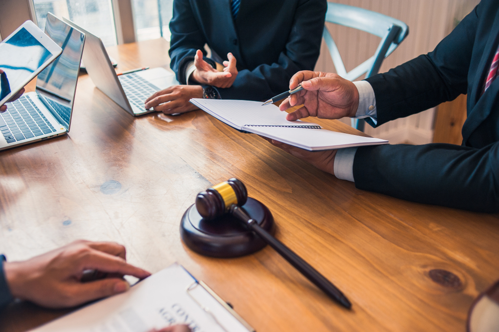 Solicitors providing legal advice to victim of police misconduct. They are holding documents and sat a large wooden table, with a gavel sat in the middle 