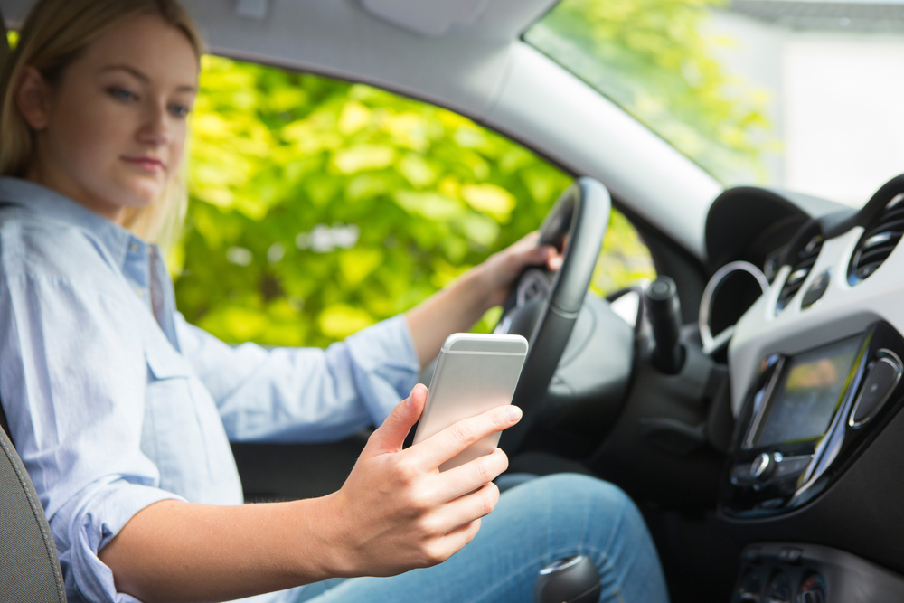 Photograph of woman in white shirt using her phone to video call whilst driving