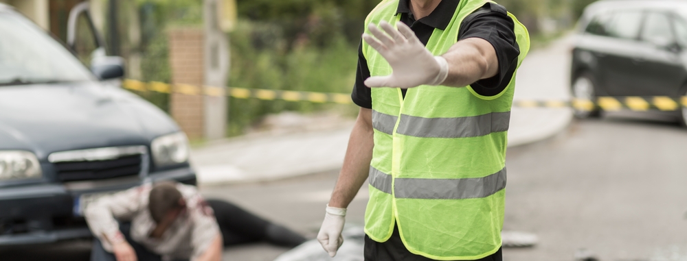 Photograph of a policeman with his hand up preventing civilians from walking onto fatal accident crime scene