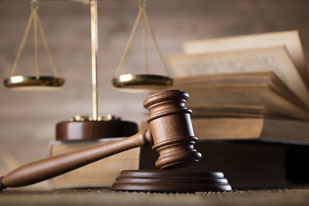 Close-up photograph of judge gavel next to legal books and scales of justice on a wooden desk