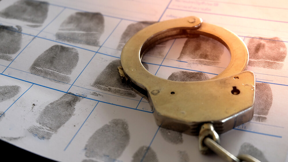 Colour image of a pair of handcuffs lying on top of a police crime file page of fingerprints