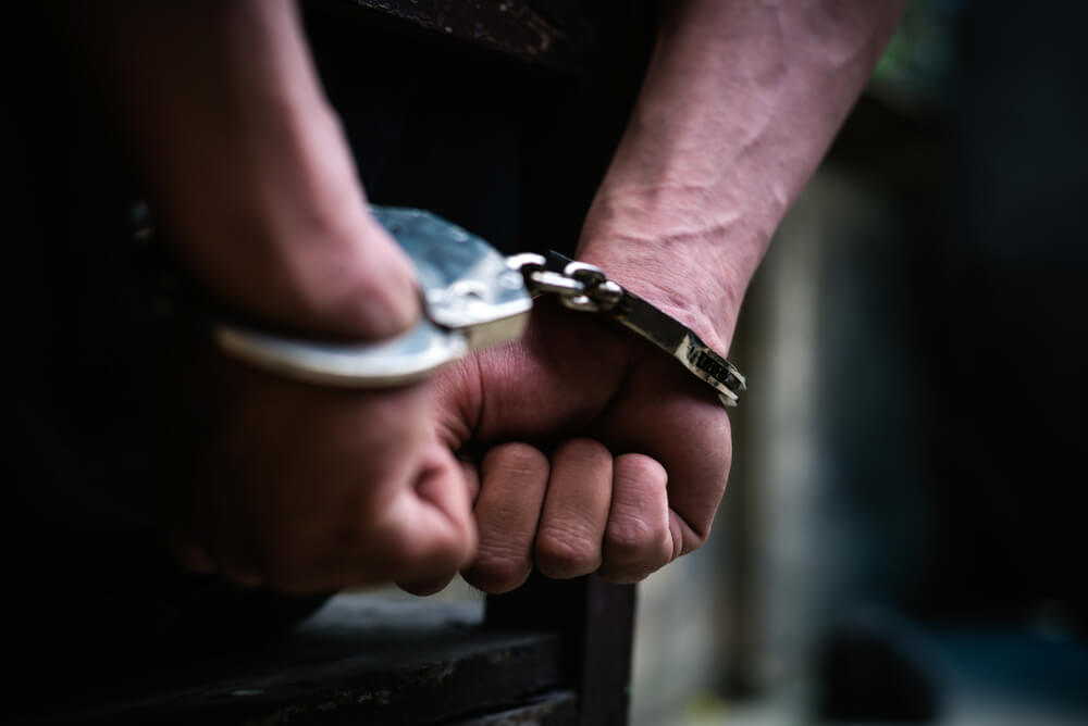 Close up image of a mans hands in handcuffs sat on a chair with fists clenched