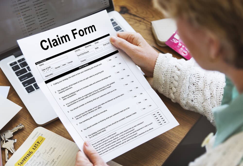 A colour image of an older woman holding a blank white claim form with black writing titled 'Claim form' 