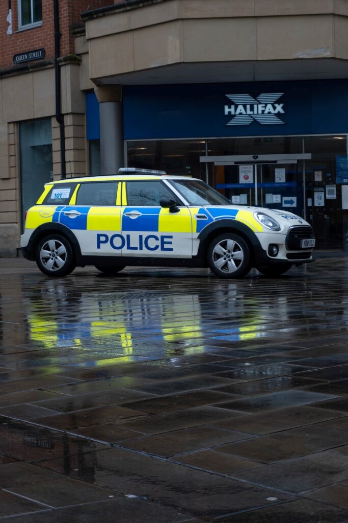 A police car parked outside a branch of Halifax bank on a rainy street.
