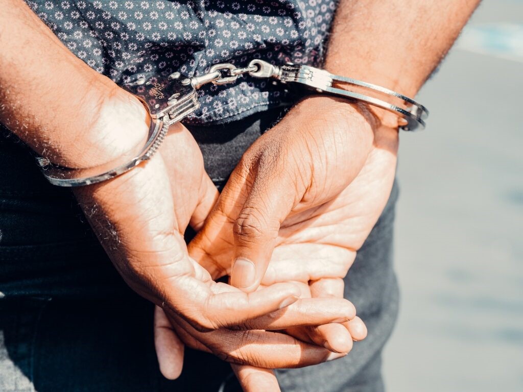 A close-up of handcuffed hands behind a persons back, with a blue spotted shirt visible above.