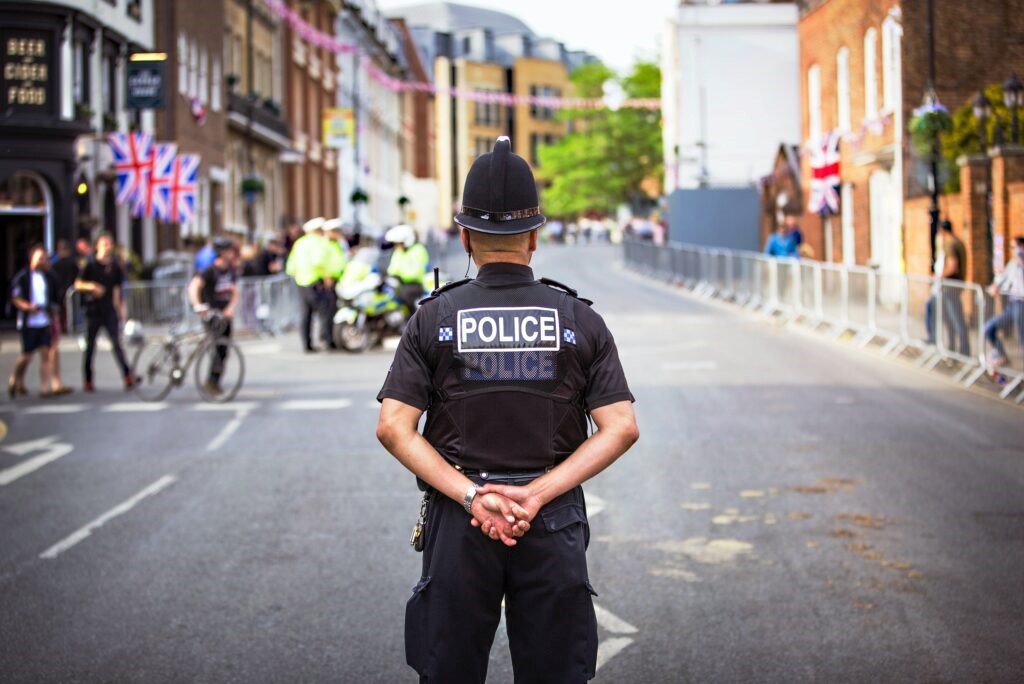 A police officer in black facing away from the camera in the middle of an empty street with metal barriers on each side.