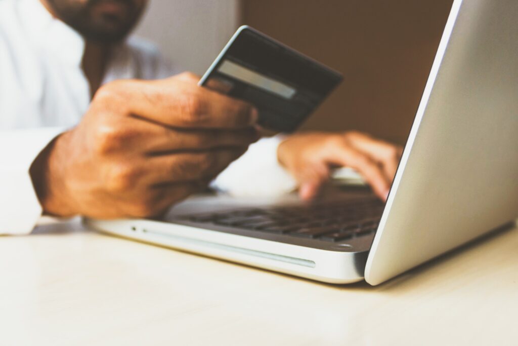 A man holding a debit card up in front of an open laptop.