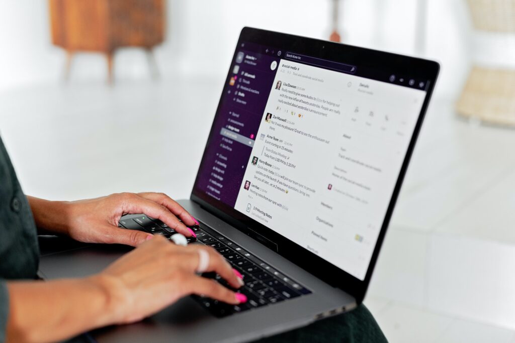 A woman's hands typing on a laptop with Slack open on the screen.