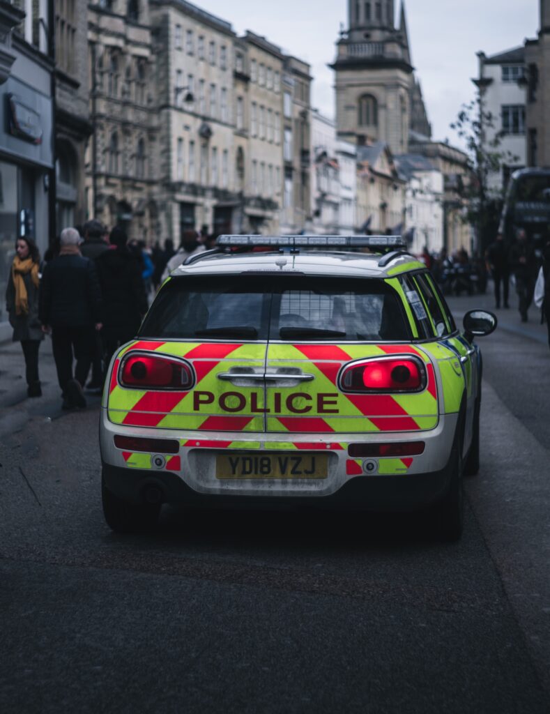 The back of a police car with yellow and orange highlighting driving down a pedestrianised street.